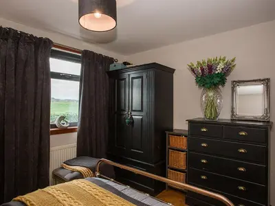 a bedroom with a cabinet and a dresser and a window at Woodend in Maxwelltown