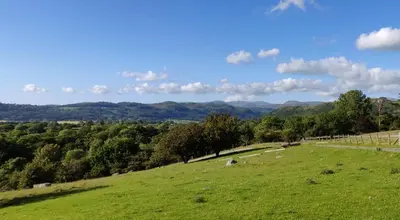 a green field with trees and mountains in the background at Row Farm Cottage in Millom