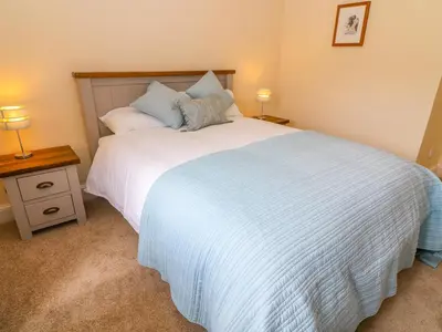 a bedroom with a large white bed and a night stand at Tilberthwaite Farm Cottage in Coniston