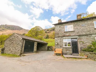 an old stone house with a bench in front of it at Tilberthwaite Farm Cottage in Coniston