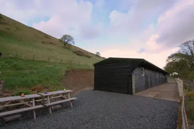 a black shed with two benches next to a hill at The White Horse Inn Bunkhouse in Threlkeld