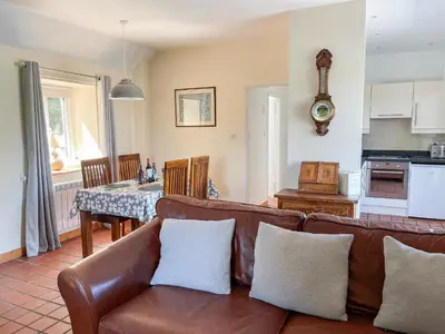 a living room with a brown couch and a kitchen at The Smiddy in Glasserton