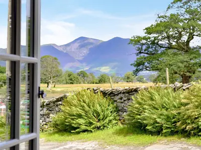 a window with a view of a stone wall and mountains at Field House Bothy - Uk12571 in Borrowdale Valley
