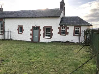 a white house with brown windows and a yard at Laundry Cottage in Dumfries