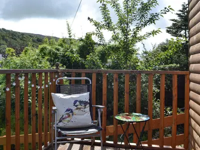 a chair with a pillow and a table on a deck at Curlew Cottage in Creetown