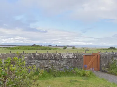 a stone wall with a wooden gate and a field at Ardlochan Cottage in Maidens