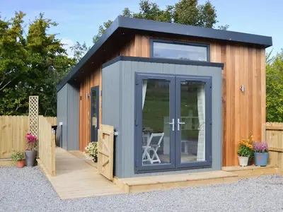 a small shed with a glass door on a wooden deck at Lapwing in Westward
