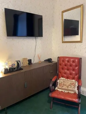 a red chair sitting in front of a dresser with a television at Rockhill Guest House in Moffat