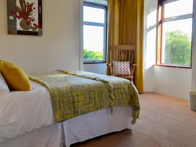 a bedroom with a bed and a chair and windows at Butterhole Farmhouse in Kelton
