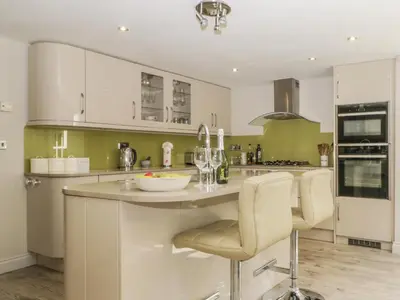 a kitchen with white cabinets and a island with chairs at Stair Cottage in Keswick