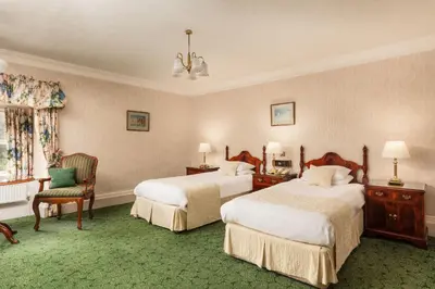 a hotel room with two beds and a chair at Cally Palace Hotel & Golf Course in Gatehouse of Fleet