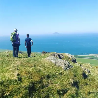 two people standing on top of a hill looking at the ocean at Woodland Bay Hotel in Girvan