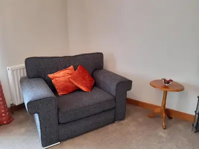 a gray chair with two orange pillows in a room at Leafield Holiday Home in Stranraer