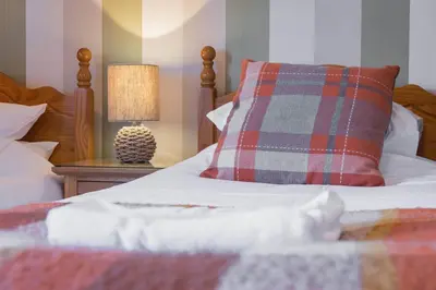a bed with a plaid pillow and a lamp on a table at Big White House in Cockermouth