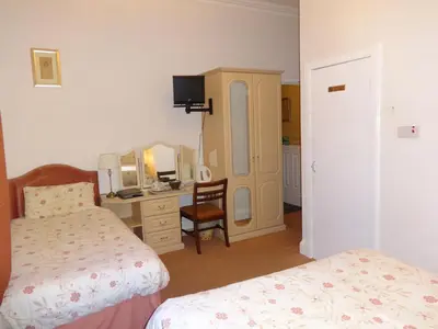 a bedroom with two beds and a desk with a mirror at Aberdour Guest House in Dumfries