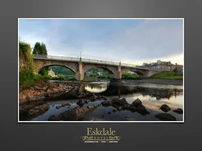 a bridge over a river with rocks in the water at Eskdale Hotel in Langholm