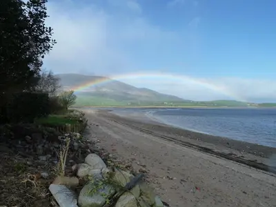 a rainbow over a beach with a road and water at Sunset Retreat Lodge with Hot Tub in Carsethorn