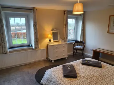 a bedroom with a bed and a television and two windows at Lovely Cottage on Hadrians Wall 12 Miles From Carlisle in Carlisle