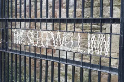 a metal fence with graffiti on the side of it at The Sleepwell Inn in Workington