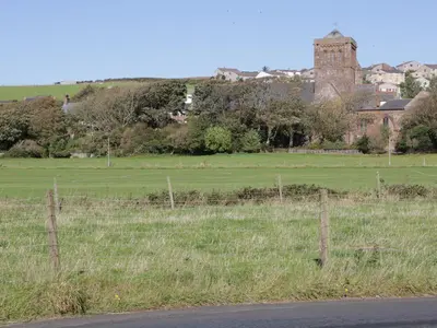 a field with a fence and a building in the background at Rowan Cottage in St Bees