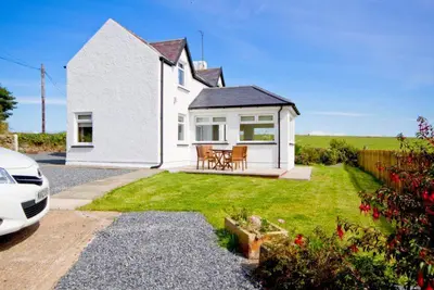 a white house with a table and chairs in the yard at Castlemoor Holiday Cottage, Mull of Galloway in Drummore
