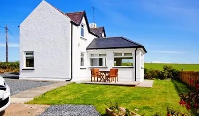 a white house with a table and chairs in the yard at Castlemoor Holiday Cottage, Mull of Galloway in Drummore