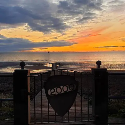 a view of a sunset from a beach with a gate at THE OLD FARMHOUSE in Holmrook