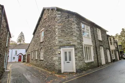 a stone building with a white door on a street at Old Bakers Cottage ground floor apartment centrally located in Grasmere with patio area in Grasmere