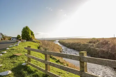 a wooden fence next to a river next to a road at 2 Whiterow in Powfoot