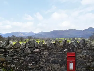 a red phone box in a stone wall with a field and mountains at Apple Barn in Applethwaite