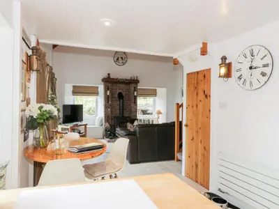 a living room with a table and a clock on the wall at The Barn in Dalbeattie