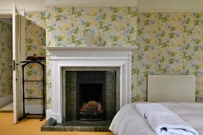 a fireplace in a bedroom with floral wallpaper at Finest Retreats - Edwardian Country House - 9 Bed, Sleeping up to 21 in Longtown