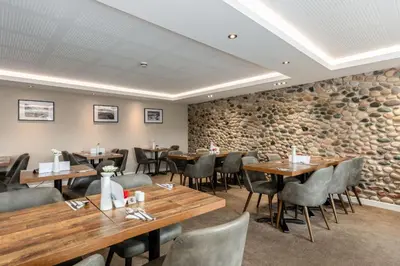 a restaurant with wooden tables and chairs and a stone wall at Seacote Hotel in St Bees