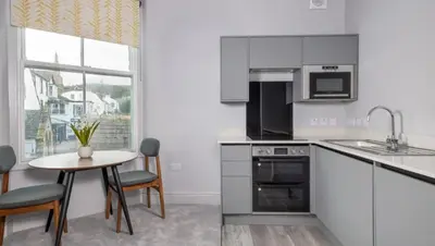 a kitchen with white cabinets and a small table with chairs at Keswick Lake Road Apartments in Keswick