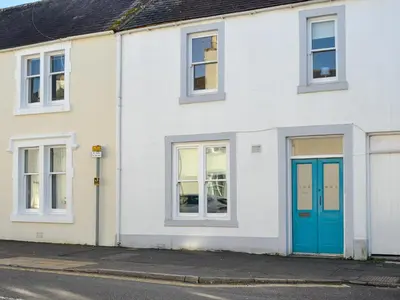 a white house with a blue door on a street at Buckle House in Gatehouse of Fleet