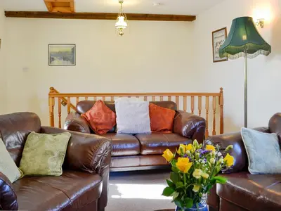 a living room with a brown leather couch and flowers at Swallows Return in Whitehaven