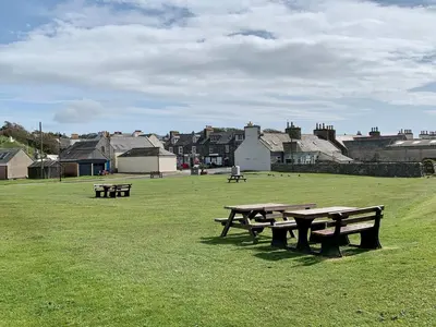 three picnic tables in a field with houses in the background at Saltlife Cottage in Port William