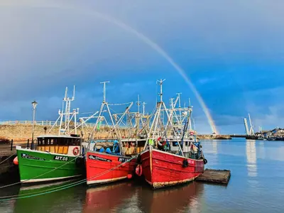 three boats are docked in the water with a rainbow at Ritson Wharf in Maryport