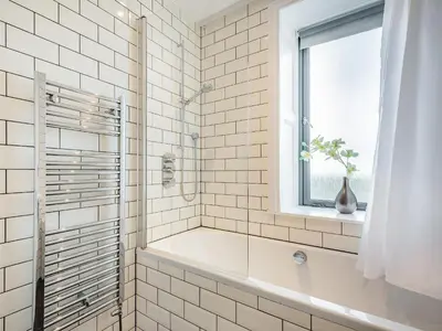a white tiled bathroom with a tub and a window at Killantrae Burn in Port William