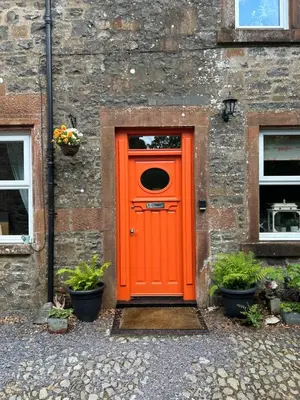 an orange door on the side of a brick building at Fox Cottage in Moffat