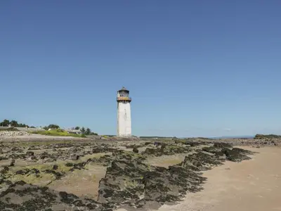 a lighthouse on a rocky beach with the ocean in the background at Sandpiper in Dumfries