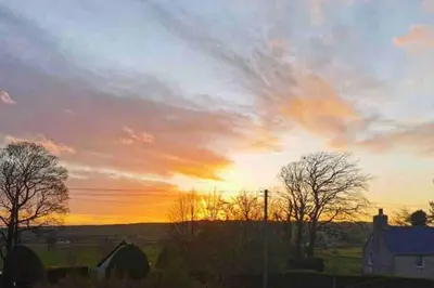a sunset over a field with a house and trees at 2 Calgow Cottages in Newton Stewart