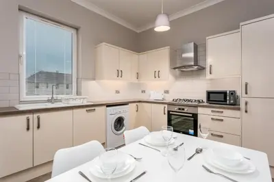 a kitchen with white cabinets and a white table and chairs at Seaforth Suite - Donnini Apartments in Ayr