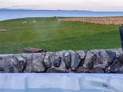 a stone wall with sheep in a field with the ocean at Bel-Mar in Whithorn