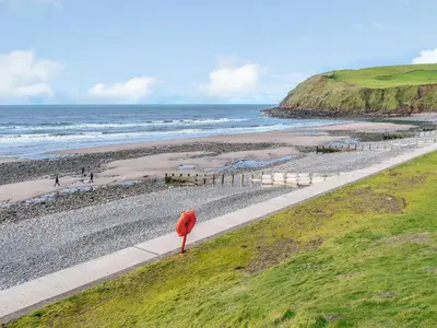 a beach with a red umbrella next to the ocean at Seacote Gardens in St Bees