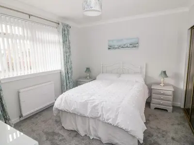 a white bedroom with a bed and two night stands at Honesty Cottage in Girvan