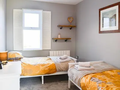 a bedroom with two beds and a desk and a window at Broomlands Cottage in Beattock