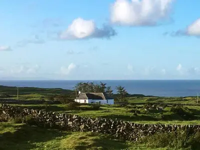 a white house in a field near the ocean at Garrarie Cottage in Monreith