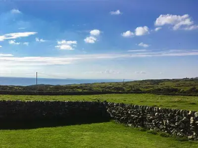 a stone fence in a green field with a blue sky at Garrarie Cottage in Monreith