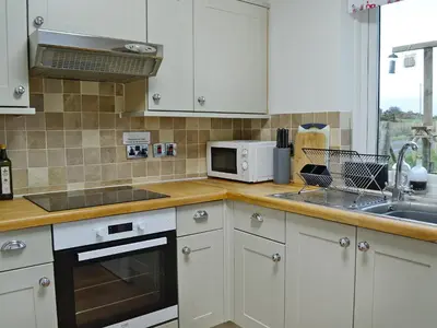 a kitchen with white cabinets and a sink and a microwave at Kirklauchline Cottage in Portpatrick